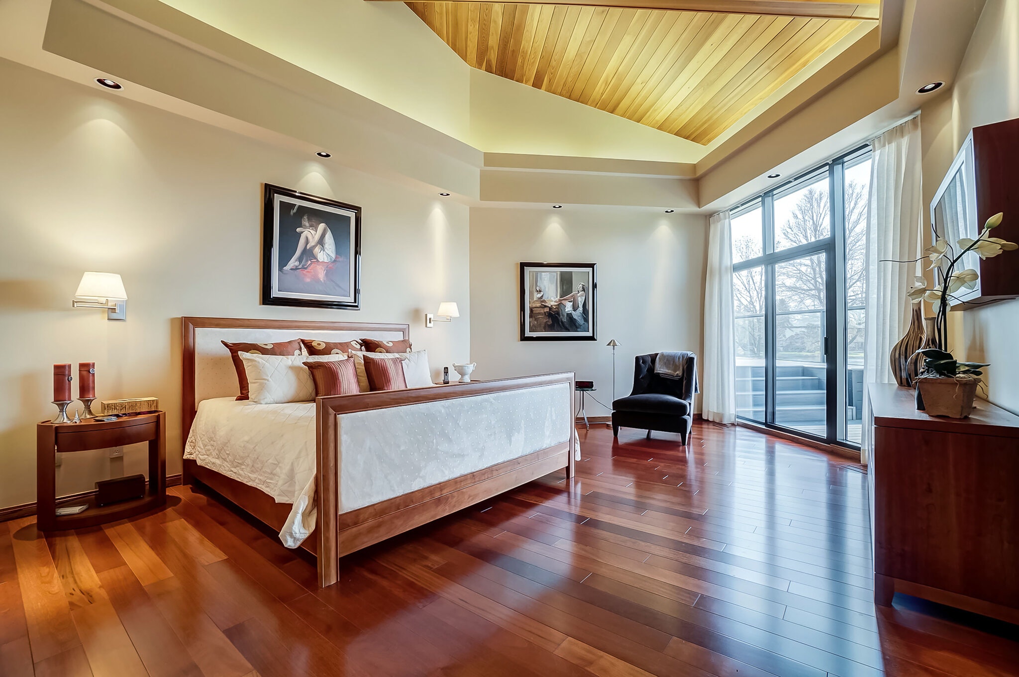 The angled ceiling in the main bedroom suite repeats the wood-beamed design in the great room. The suite connects to a deck through a patio door.