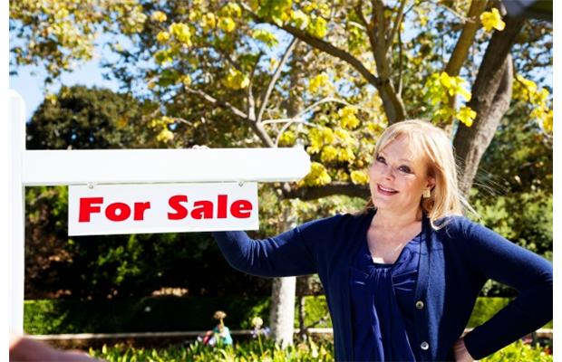 a woman holding a home for sale sign